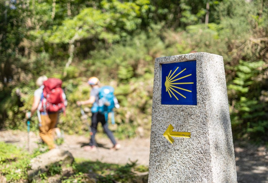 Pilgrims walking on their way to Santiago de Compostela. Camino de Santiago milestone sign on forest scene